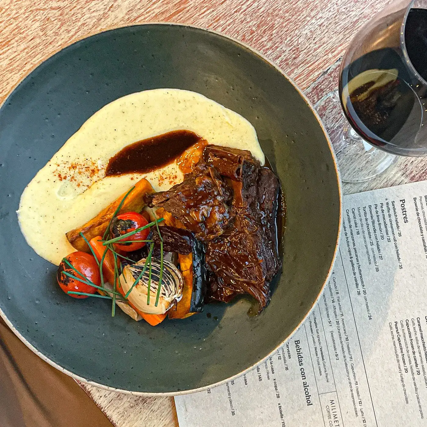 Res de larga cocción de mó en su jugo, con puré y verduras asadas, servida sobre mesa de madera